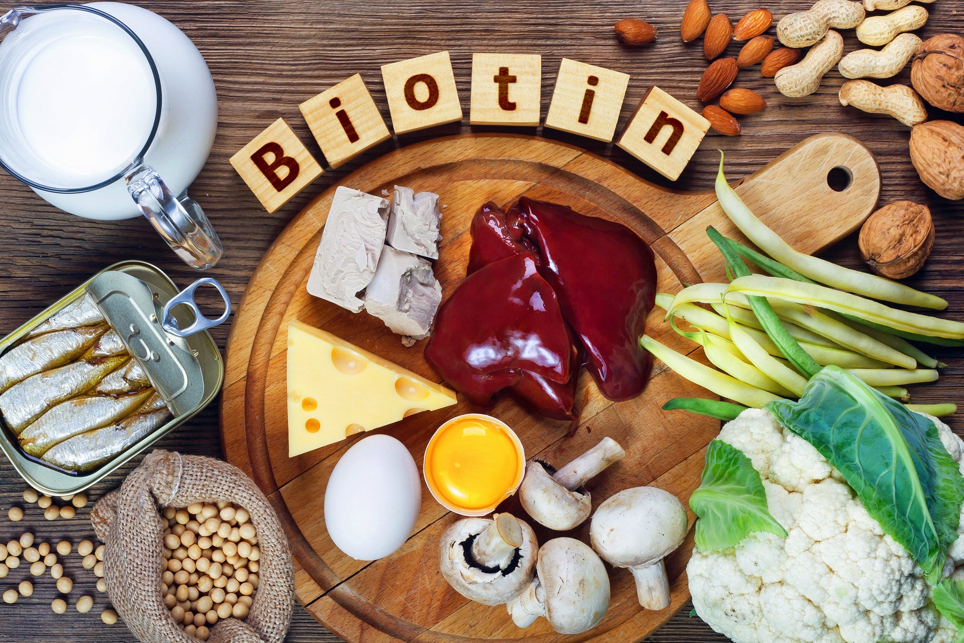 Biotin-rich foods, including liver, eggs, nuts, and milk, on a wooden table.