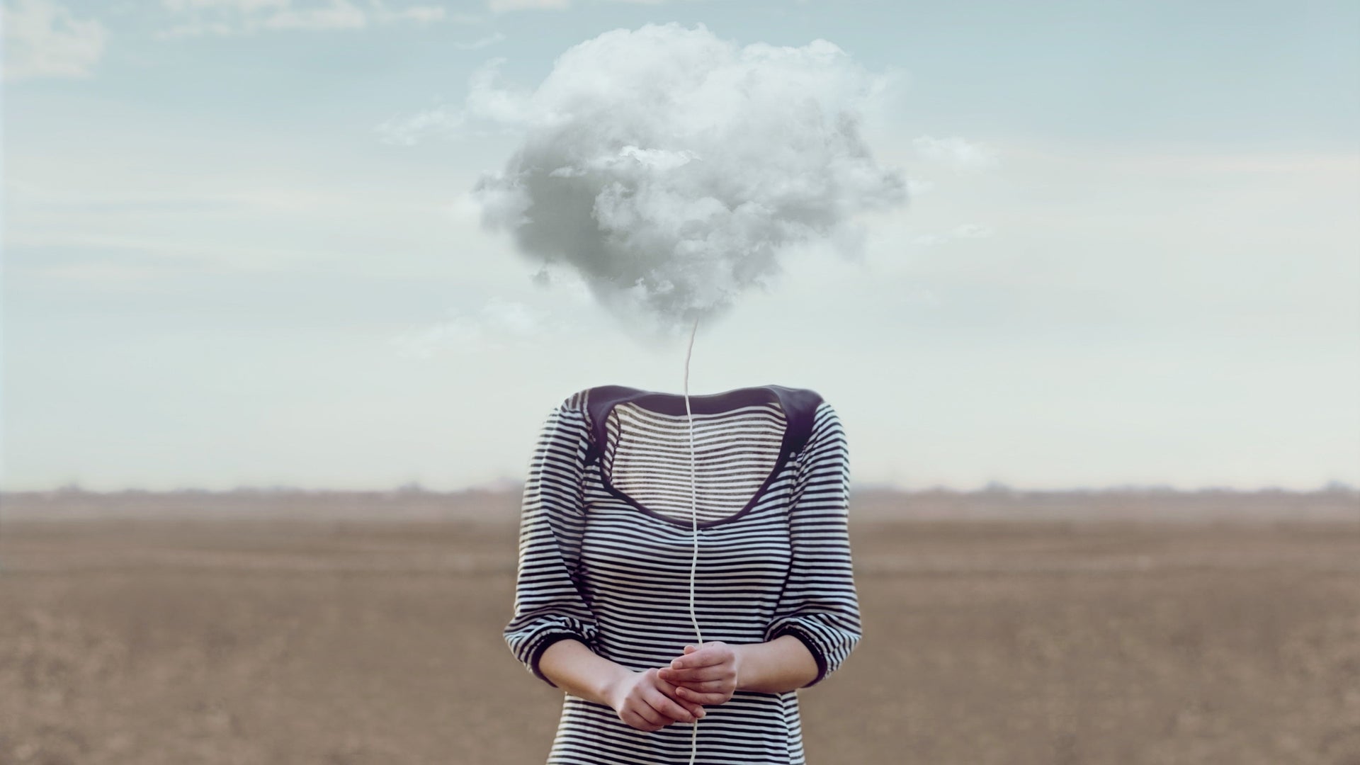 Person with a cloud for a head in an open field, wearing a striped shirt.