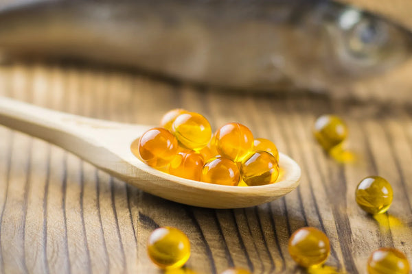 Wooden spoon with golden oil capsules on table.