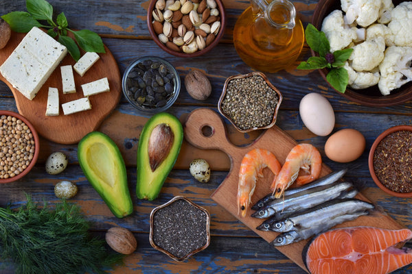 Assorted healthy foods with avocados, nuts, eggs, seafood, and tofu on a rustic table.