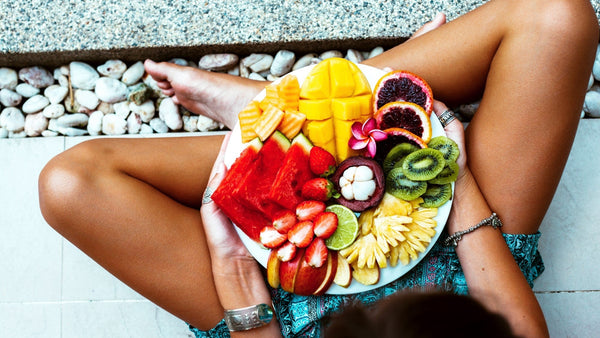 Plate of colorful fresh fruits on lap, outdoors setting.