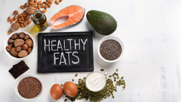 Healthy fats including salmon, avocado, nuts, and seeds on a table