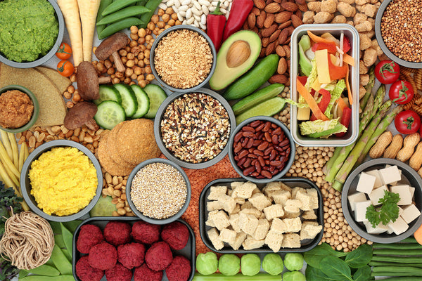 Variety of plant-based foods including nuts, seeds, grains, and vegetables displayed in bowls.