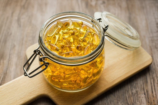 Glass jar filled with yellow supplement capsules on wooden board.