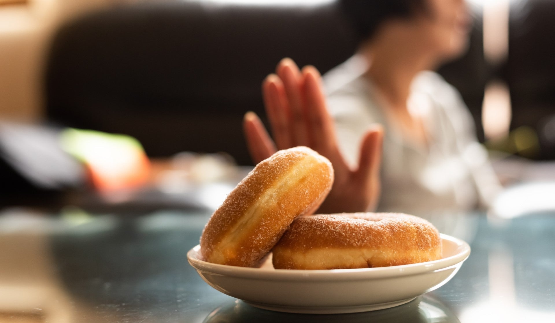 Person rejecting plate of glazed donuts on the table.