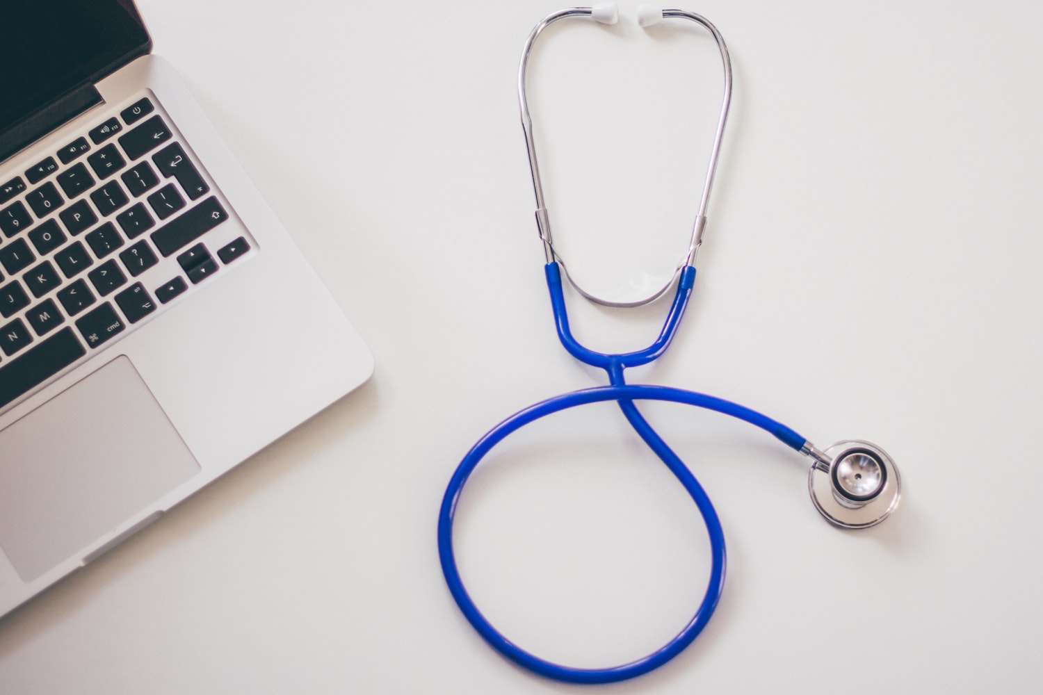 Laptop and blue stethoscope on white desk, symbolizing healthcare technology integration.