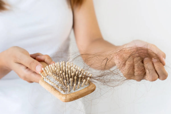 Person holding hairbrush with hair, experiencing hair loss.