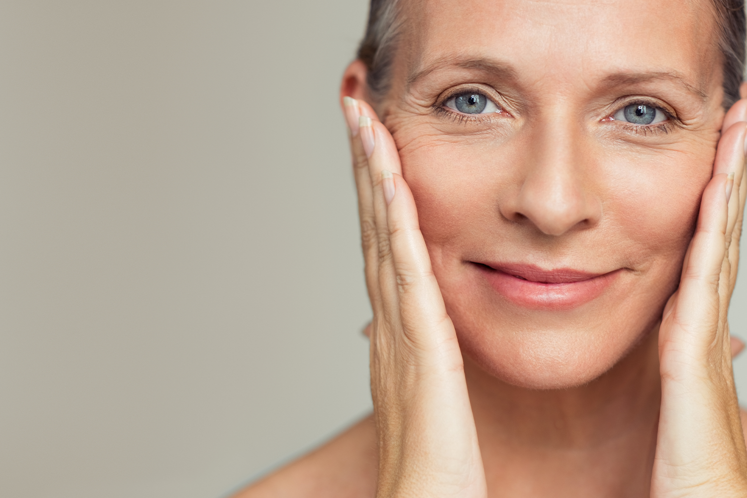 Smiling mature woman touching her face, showcasing healthy skin.