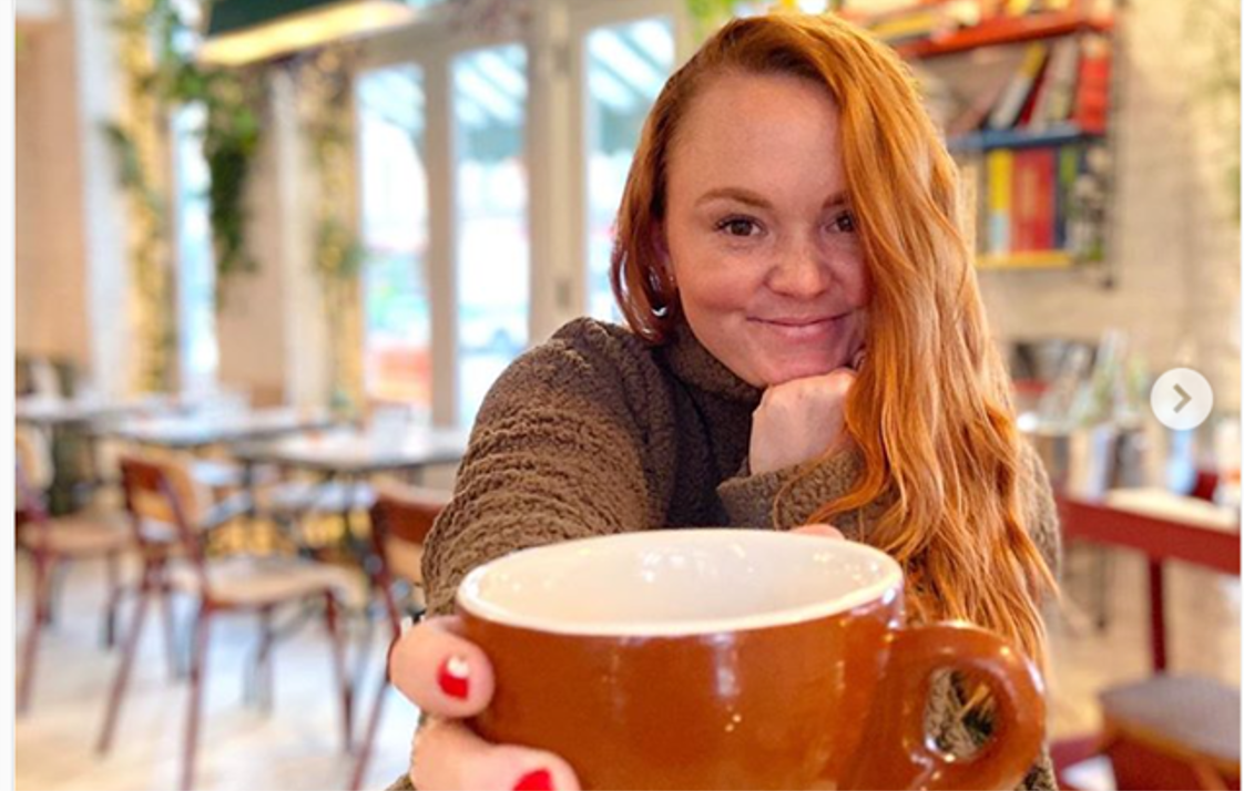 Woman enjoying coffee in a cozy cafe, smiling and holding a large brown mug.